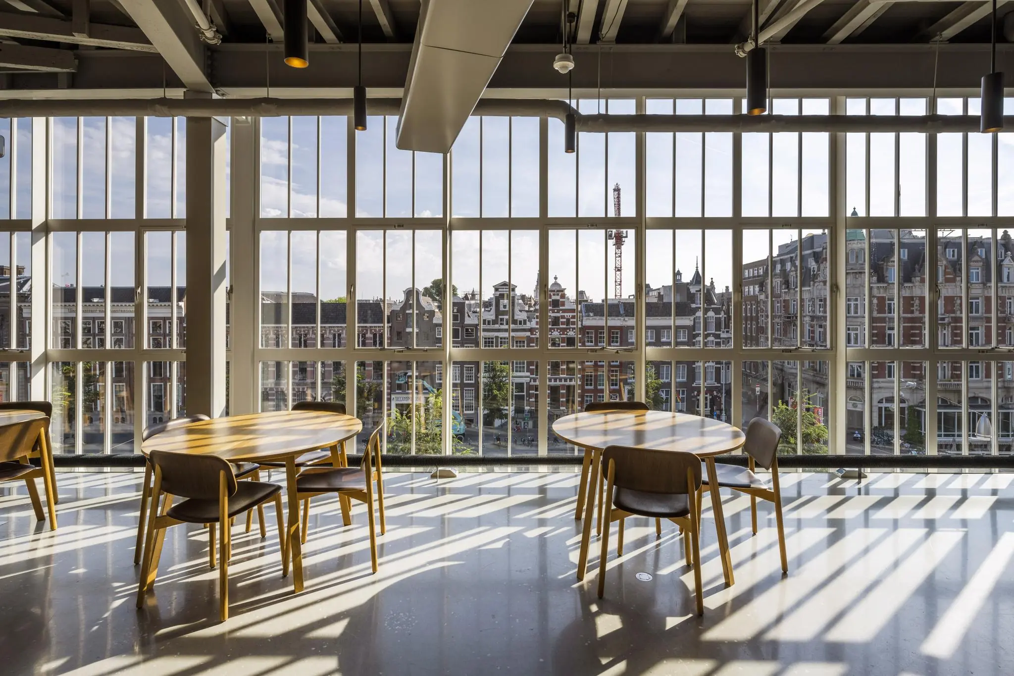 Zitgedeelte met houten tafels en stoelen in een modern interieur met uitzicht op de Sint-Jorissteeg en historische panden in Amsterdam.